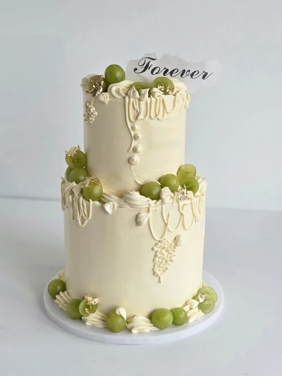Two-tier ivory drip cake with green grapes, edible gold leaf and Forever topper